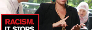 woman explaining something to 2 other people sitting at her table includes Racism It Stops With Me logo and the words, 'if you witness it, speak up'