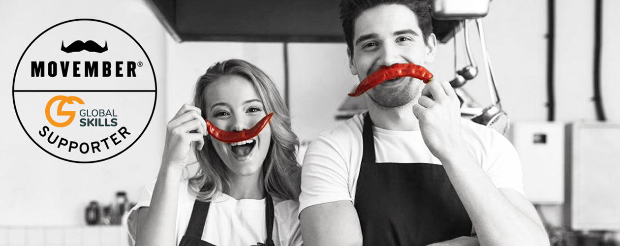 a man and woman standing in kitchen each holding a chilli in place of a moustache