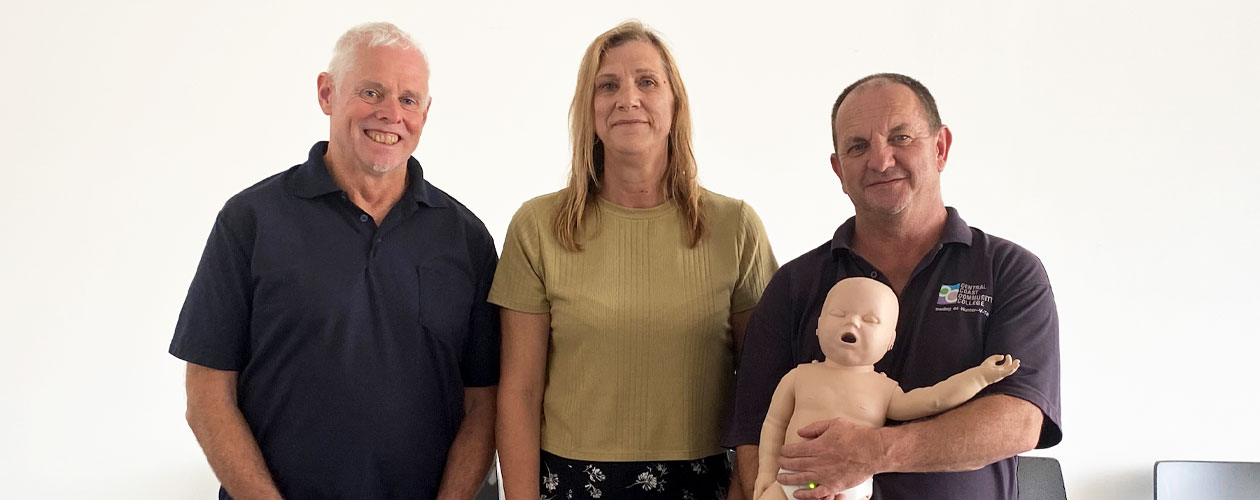 Global Skills job seeker and staff member standing with First Aid trainer holding CPR doll