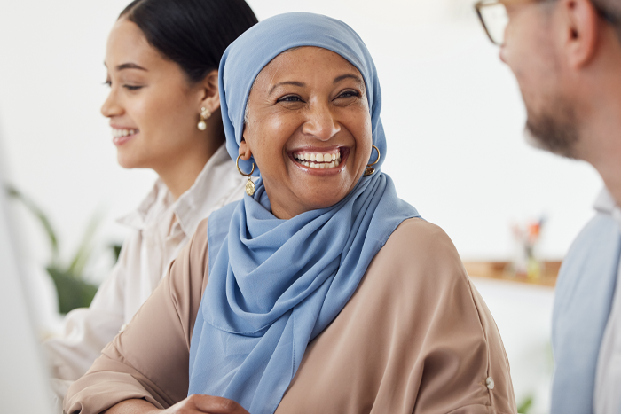 lady with hijab sitting at table smiling at person next to her