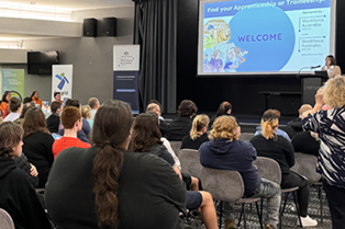 young people sitting on chairs listening to a presentation by an employer at the event