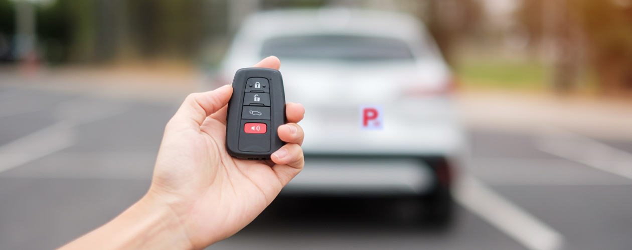 hand holding key fob with grey car including p-plate in background