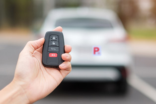 hand holding key fob with grey car including p-plate in background