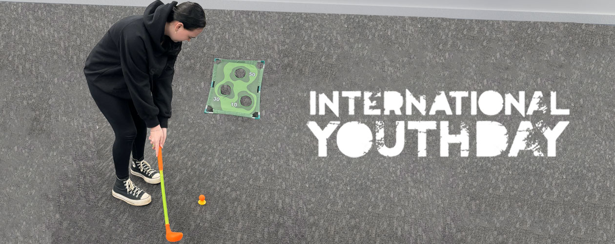 A young person holding a plastic golf club lining up to hit a ball towards a target