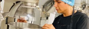 Javid, wearing a hairnet and looking into a large mixing bowl