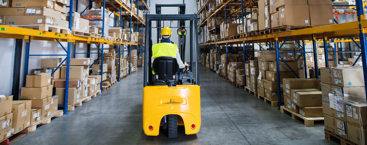 A forklift operator navigates a warehouse aisle, with high shelves stacked with boxes on both sides