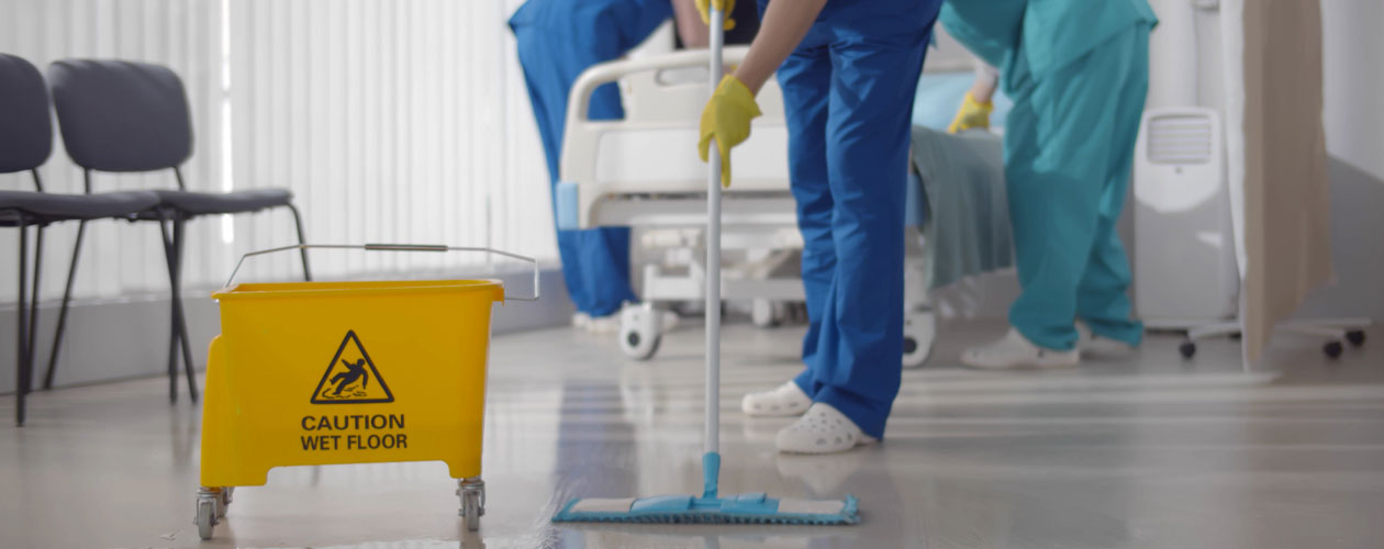 Hospital cleaner mopping the floor includes sign ‘caution wet floor’