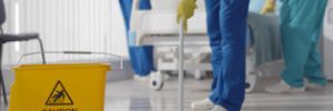 Hospital cleaner mopping the floor includes sign ‘caution wet floor’
