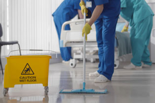 Hospital cleaner mopping the floor includes sign ‘caution wet floor’