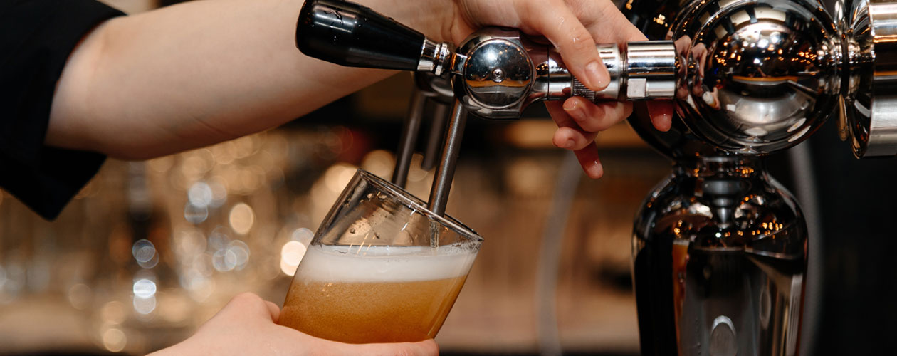 Close up view of hands using a bar tap to pour a beer