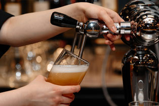 Close up view of hands using a bar tap to pour a beer