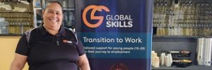 Jennifer standing behind our expo table, next to a Global Skills Transition to Work banner, with branded bottles and merchandise on display.