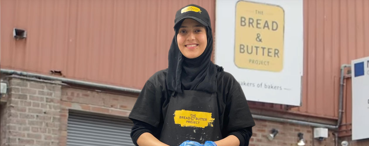 Nazila baking at The Bread and Butter Project. Her apron and hat feature the Project’s logo.