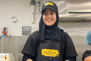 Nazila baking at The Bread and Butter Project. Her apron and hat feature the Project’s logo.