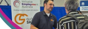 Image includes this year’s theme, “Fostering disability inclusive societies for advancing social progress,” in teal text, along with the IDPwD logo, the Inclusive Employment Australia (IEA) logo, and the Global Skills logo. On the right, a photo shows Robert at our event stall speaking with a participant. Behind them is the Global Skills IEA banner. A curved teal and magenta design separates the text and the photo.
