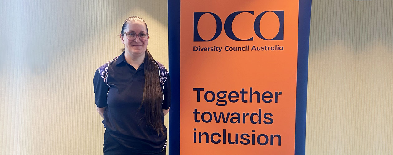 Liz stands beside a DCA banner that reads, 'Together Towards Inclusion.'