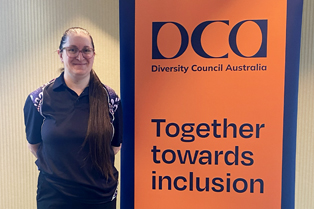Liz stands beside a DCA banner that reads, 'Together Towards Inclusion.'