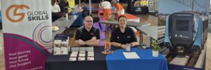 Trent and Amy seated at our stall, with Global Skills and Sydney Metro branded banners displayed behind and beside them. Promotional materials are arranged on the table