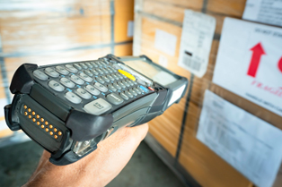 Close-up of a worker using a barcode scanner in front of stacked cardboard boxes with shipping labels. Workforce Australia and Global Skills logos appear in the bottom right corner.