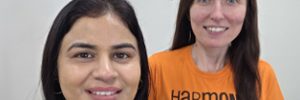 two Global Skills team members smiling at camera. one is wearing a t-shirt with the Harmony Day logo.