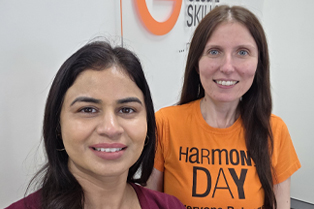 two Global Skills team members smiling at camera. one is wearing a t-shirt with the Harmony Day logo.