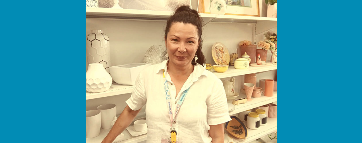Liisa at work standing beside shelves displaying homewares such as vases, bowls and plates. At the bottom of the image is a teal banner with the Workforce Australia and Global Skills logos.