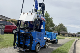 Jaycob’s blue remote-control truck is parked on a footpath, next to a road.