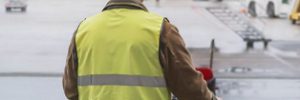 A worker in a high-visibility vest pushing a cleaning cart across an airport tarmac. Workforce Australia and Global Skills logos appear in the bottom right corner.