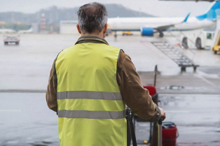A worker in a high-visibility vest pushing a cleaning cart across an airport tarmac. Workforce Australia and Global Skills logos appear in the bottom right corner.