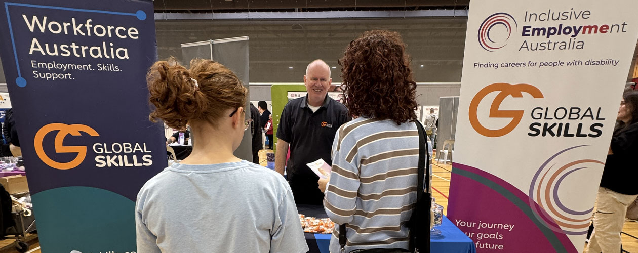 Global Skills Manager Simon speaking with attendees at our expo stall, featuring Global Skills’ Workforce Australia and Inclusive Employment Australia banners.