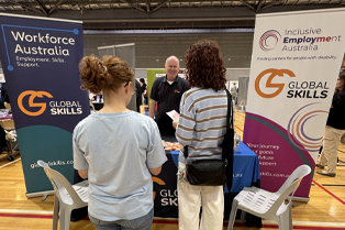 Global Skills Manager Simon speaking with attendees at our expo stall, featuring Global Skills’ Workforce Australia and Inclusive Employment Australia banners.