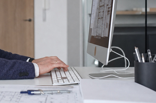 A person working at a desktop computer with architectural plans and drafting tools on a desk. Workforce Australia and Global Skills logos appear in the bottom right.