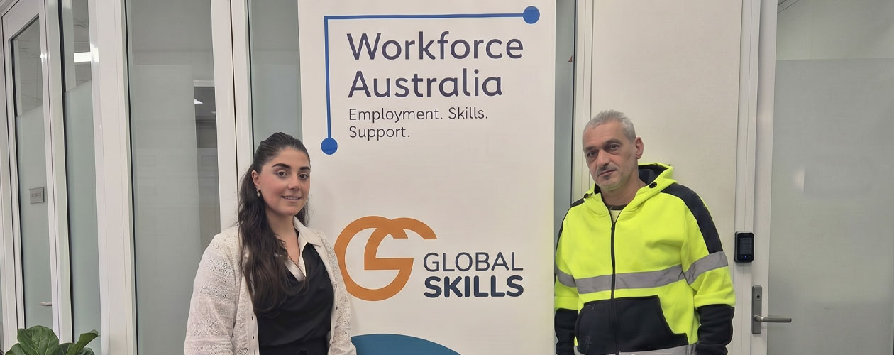 Natasha and Raad standing either side of a Global Skills Workforce Australia banner. Raad is wearing high-visibility workwear.