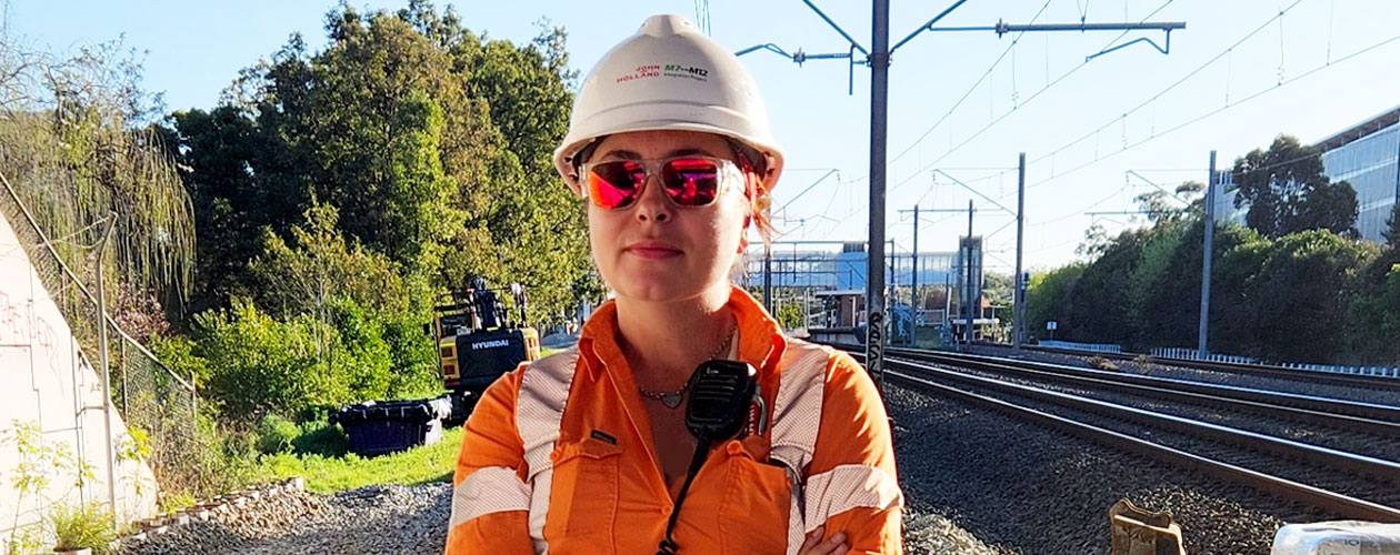 Hayley standing on railway tracks wearing high visibility clothing and a hard hat.