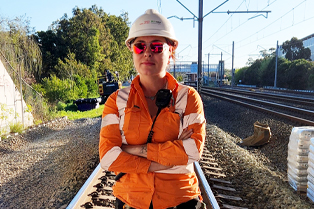 Hayley standing on railway tracks wearing high visibility clothing and a hard hat.