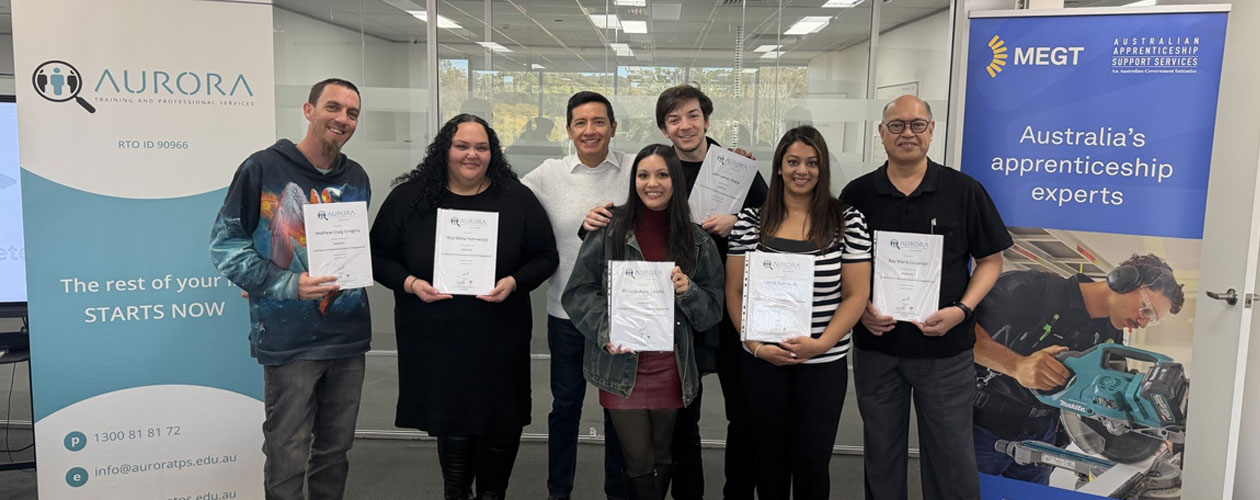 Our graduates proudly holding their certificates alongside their trainer, Pavel. They are pictured in front of MEGT and Aurora Training Institute banners.