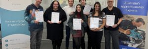 Our graduates proudly holding their certificates alongside their trainer, Pavel. They are pictured in front of MEGT and Aurora Training Institute banners.