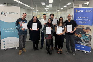 Our graduates proudly holding their certificates alongside their trainer, Pavel. They are pictured in front of MEGT and Aurora Training Institute banners.