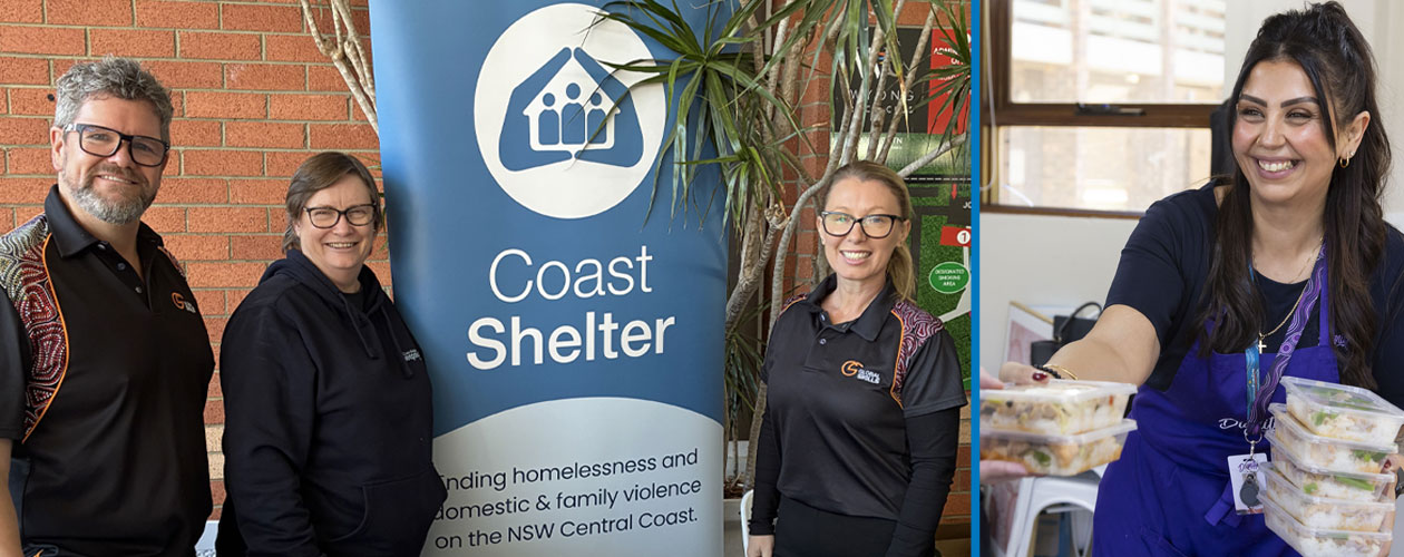 Martin and Racheal from Global Skills with Penny from Coast Shelter, standing beside a Coast Shelter banner plus a Dignity volunteer smiling while holding containers of prepared meals.