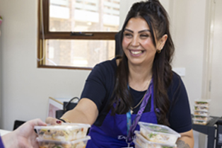 A Dignity volunteer smiling while holding containers of prepared meals