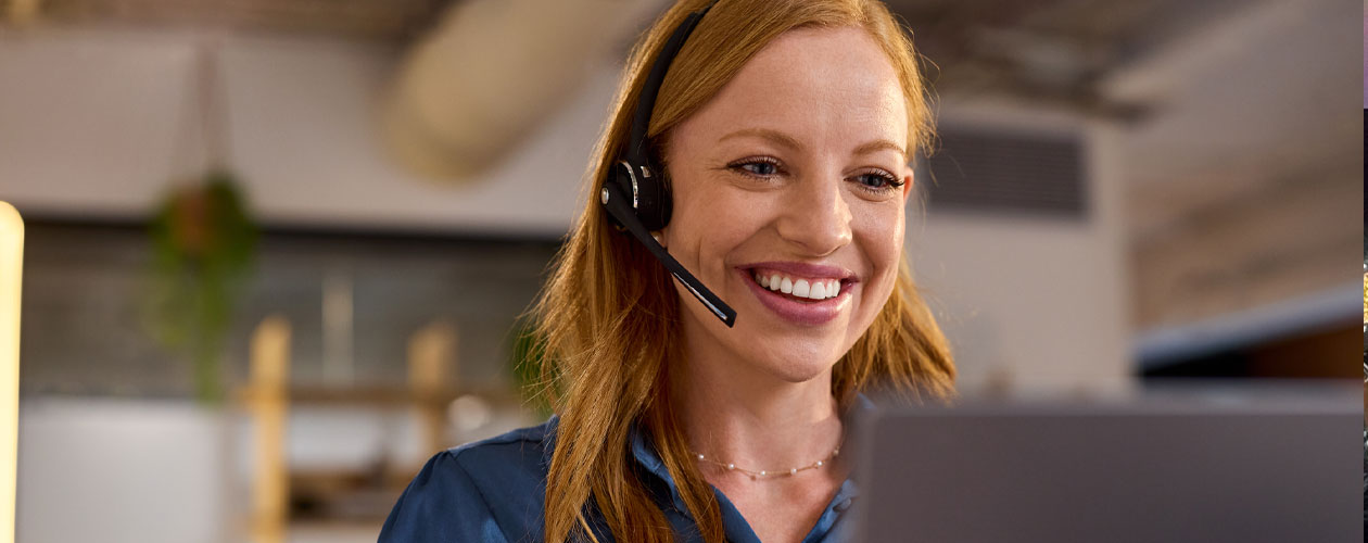 A woman wearing a black headset and blue blouse is seated at a computer in an office environment. A laptop is visible in the foreground. Workforce Australia and Global Skills logos appear in the lower right corner.