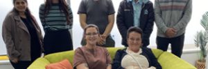 A group of attendees smile for a group photo, with two women seated on a bright green sofa and five people standing behind them. Global Skills and Workforce Australia logos appear at the bottom.