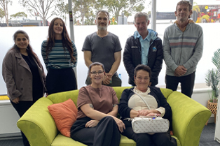 A group of attendees smile for a group photo, with two women seated on a bright green sofa and five people standing behind them. Global Skills and Workforce Australia logos appear at the bottom.