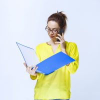 Girl holding a blue folder and positively talking to the phone. High quality photo